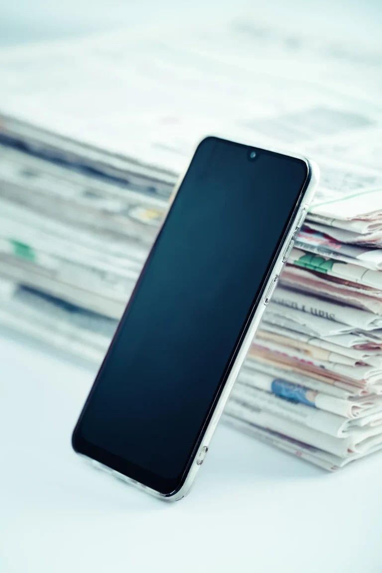 Ein Smartphone lehnt an einem Stapel Zeitungen