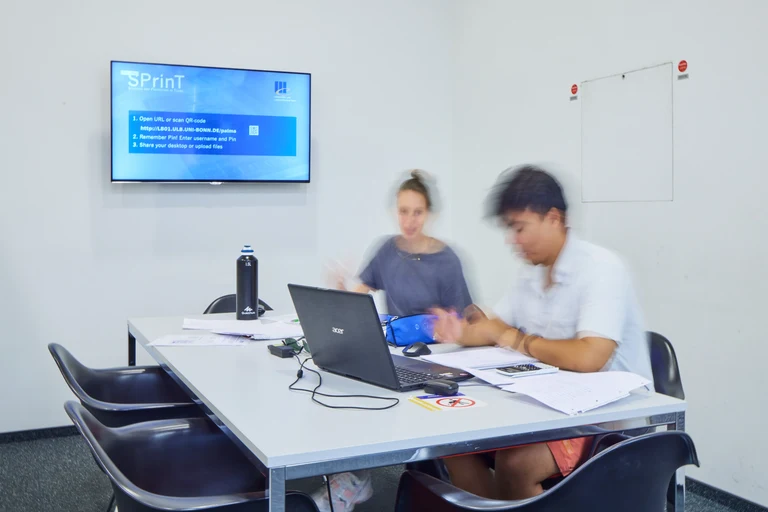 Zwei Studierende arbeiten gemeinsam mit Laptops am Gruppenarbeitsplatz.
