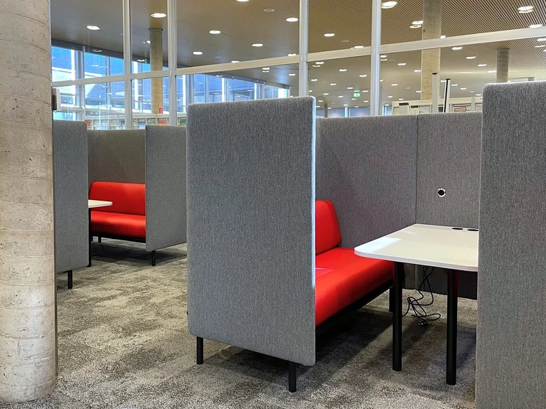 Gruppenarbeitsplätze mit je einem Tisch und Sitzbänken, die mit schalldämpfenden Stoffwänden voneinander abgetrennt sind.